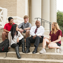 A group of students sitting on steps chatting with the University's Vice President.